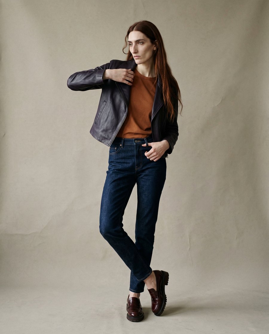 A model in a leather jacket and dark denim against a paper studio backdrop